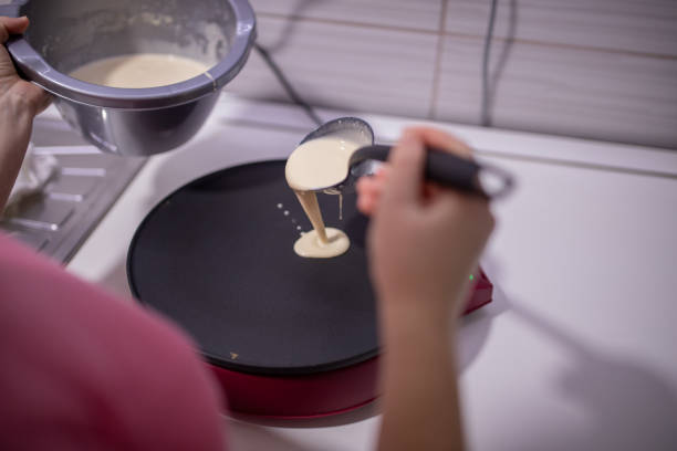 Housewife preparing breakfast for family, she is pouring pancake batter on electric pancake maker