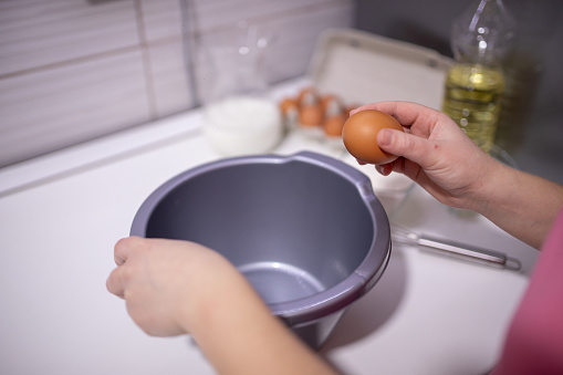 Preparing pancakes. Woman hands breaking a raw egg