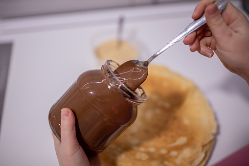 Young woman making French pancakes filled with Chocolate Cream and biscuit crumbs at home