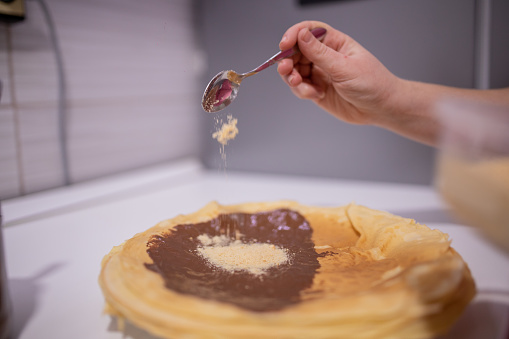 Young woman making French pancakes filled with Chocolate Cream and biscuit crumbs at home