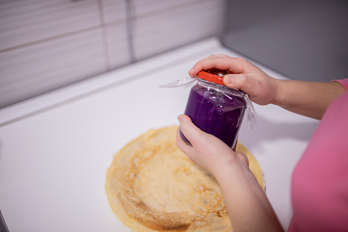 Woman spreading jam on French pancakes, hands shown, crepes with jam