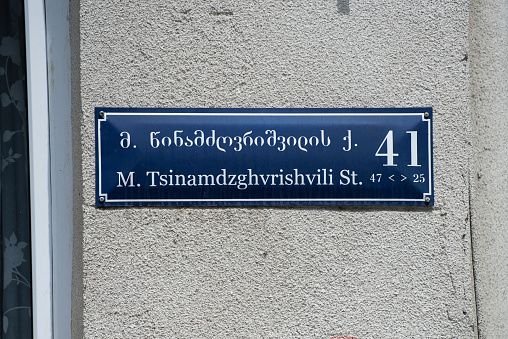 Street sign and name in Georgian and transliterated English, mounted to a cement wall in Tbilisi, Republic of Georgia.