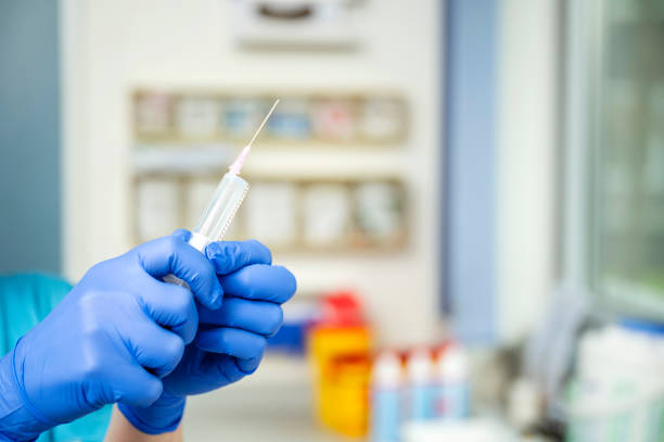 A doctor wearing blue protective gloves draws up a syringe with a clear liquid.