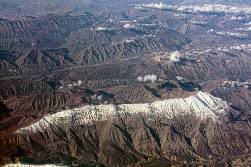 Aerial view of a single snow-capped mountain range surrounded by dry mountains