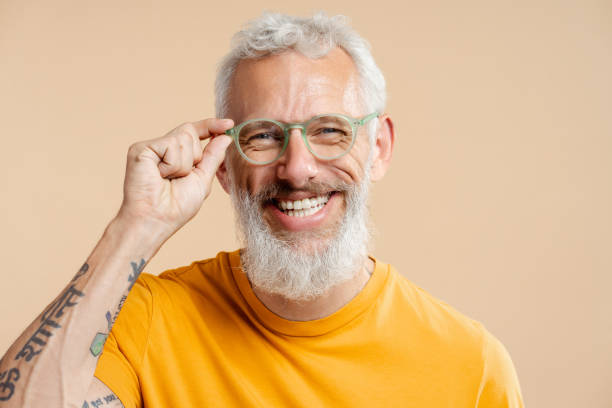 세련된 안경과 노란색 티셔츠를 입은 성공적인 성숙한 남자, 베이지색 배경에 고립 - scandinavian men glasses shirt 뉴스 사진 이미지