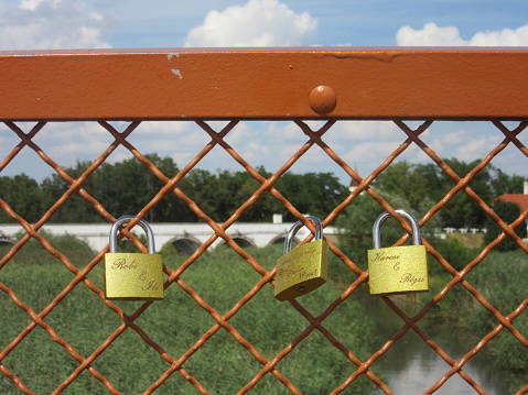 Love padlocks on a metal fence with the Nine-arched bridge ( Kilenclyukú híd ) visible in the background, in Hortobágy, Hungary
