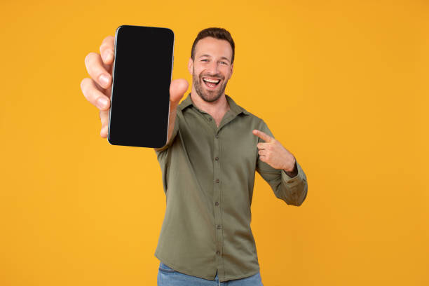 istock Excited caucasian man holding blank cellphone showing screen to camera pointing at it, recommending website or application, mockup banner 2102643717