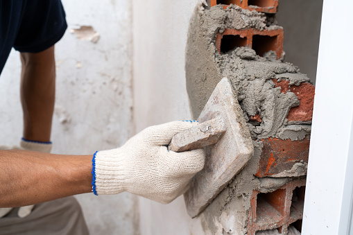 Close-up view of a construction worker's hands placing bricks and applying cement at a building site.