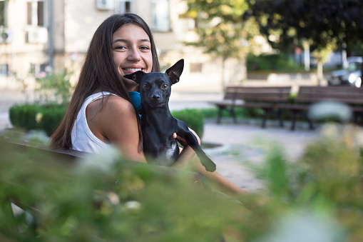Cute portrait of a happy smiling teenage girl having fun with her dog in a park. Spending time together. Love and care.