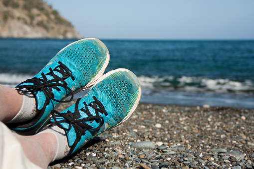 Women's legs in blue sneakers on a pebble beach against the backdrop of the sea. Sports and relaxation on the sea coast. Mediterranean Sea, Turkey, Antalya, Kemer