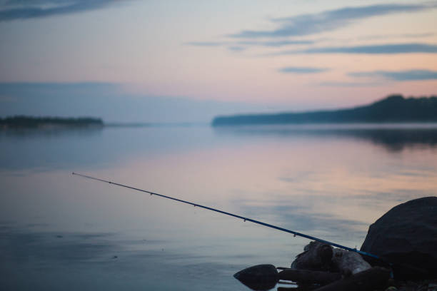 The person is peacefully fishing at dusk on the tranquil lake, surrounded by a breathtaking natural landscape of water, sky, and horizon