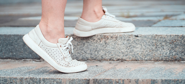 A girl walks in the city, steps of a staircase, close-up view of her feet with stylish white sneakers on, comfortable casual shoes.