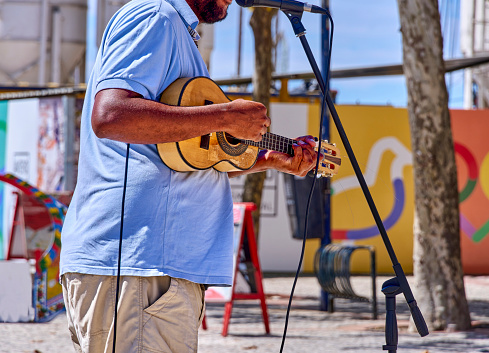 A musician plays guitar, captured mid-performance outdoors.