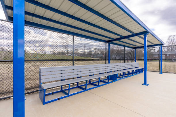 istock View of typical nondescript high school baseball softball dugout with concrete floor, chain link fence, and blue roof shade. No people visible. Not a ticketed event. 2102741196