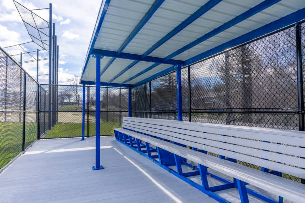 istock View of typical nondescript high school baseball softball dugout with concrete floor, chain link fence, and blue roof shade. No people visible. Not a ticketed event. 2102741252