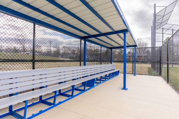 istock View of typical nondescript high school baseball softball dugout with concrete floor, chain link fence, and blue roof shade. No people visible. Not a ticketed event. 2102741523