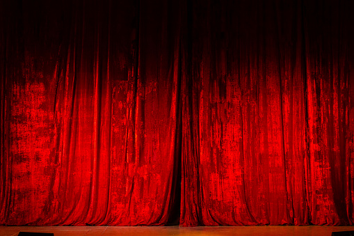Theater curtain in magenta hue hangs on the empty stage, ready to unveil the next entertainment event. The red curtain adds a bold touch to the scene