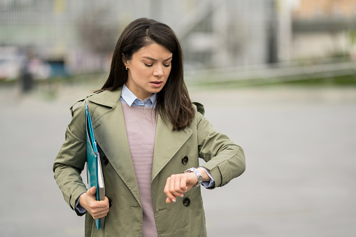 Young businesswoman looking at her watch while hurrying to work on city street.