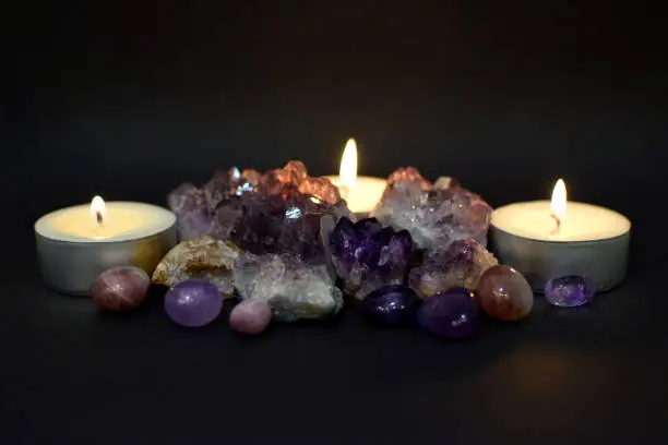 Beautiful purple druzy with amethyst crystals and burning candles in the dark. Selective focus.