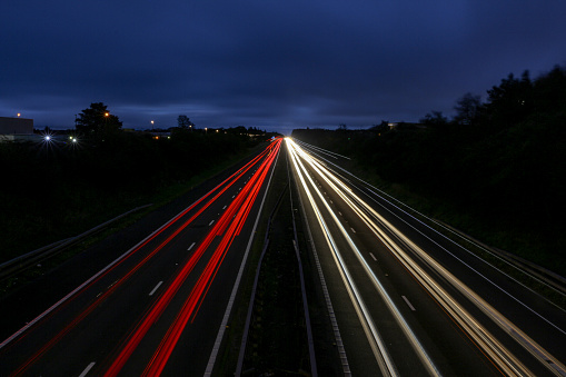 Lights of traffic passing by on a highway through nature at night. Long exposure image with light trails in white and red caused by the head and tail lights of the passing cars.