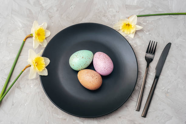 istock Black plate with Easter eggs, yellow daffodil flowers and cutlery on textured gray background. Top view, flat lay 2102825794