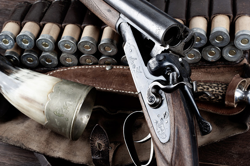 double barreled side shotgun with cartridges in bandolier on wooden table.