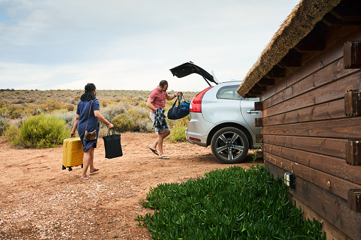Friends packing their luggage into the trunk of their car after a summer vacation together at a cabin in a nature reserve