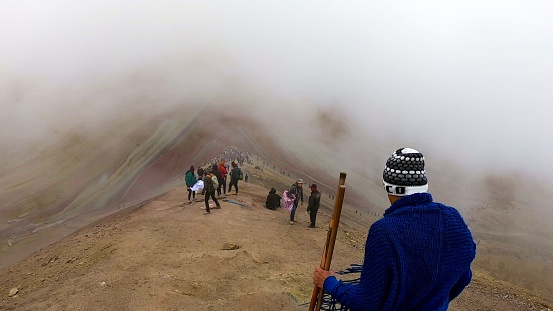 Cusco, Peru - February 9 2019 : Traveler in warm attire looks out over a foggy peak as tourists explore the colorful mountain terrain, the Rainbow mountain in Cusco - Peru