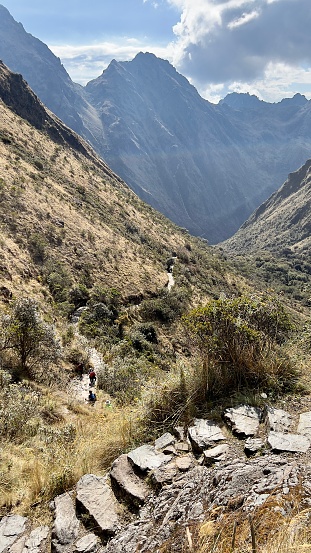 This image captures a group of hikers navigating the downward slope of the Inca Trail, having crossed the challenging Dead Woman's Pass. Surrounded by the natural landscape of the Andes, the trail curves into the valley below, where more historical sites await explorers.