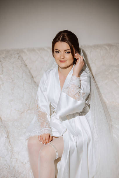 a beautiful brunette bride with a tiara in her hair is getting ready for the wedding in a beautiful robe in boudoir style. close-up wedding portrait, photo. - jewelry glamour brown hair stage makeup stock-fotos und bilder