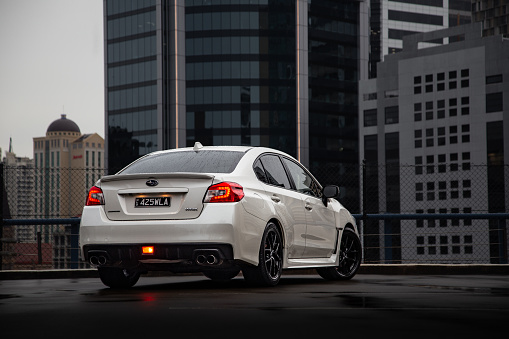 Sporty Subaru WRX sedan clicked during a creative photoshoot showing rear three-quarter with fog lamps turned on for added visibility. Cityscape views can be seen in the background.