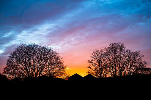 This captivating photograph captures the serene beauty of a winter sunset in Birmingham, UK. As the sun dips below the horizon, casting a warm golden glow across the sky, the silhouette of a quaint house stands in stark contrast against the wintry landscape. Surrounding the house, bare trees with branches adorned in delicate frost create a striking contrast against the fiery hues of the setting sun. The tranquil scene exudes a sense of quietude and peace, as the last light of day illuminates the snowy ground, casting long shadows and infusing the landscape with a soft, ethereal quality. Against the backdrop of the urban skyline, the juxtaposition of nature's winter beauty and the warmth of a home evokes a sense of nostalgia and wonder, inviting viewers to pause and appreciate the simple yet profound beauty of the moment.
