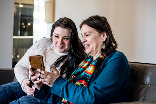 In a scene of mutual fascination, an indigenous mother and daughter bond over an intriguing discovery on a phone screen, deepening their connection through shared curiosity.