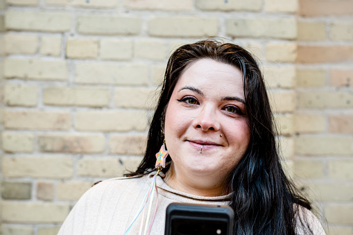 Against a rustic brick backdrop, a 28-year-old indigenous woman confidently navigates the digital landscape, her phone a portal to connectivity and empowerment.