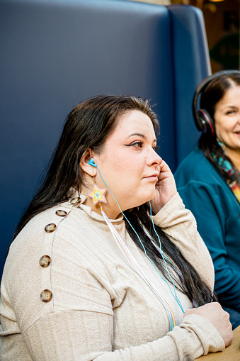In a candid scene of shared intimacy, an indigenous mother and daughter come together as the younger woman adjusts her earbuds, fine-tuning their shared musical experience.