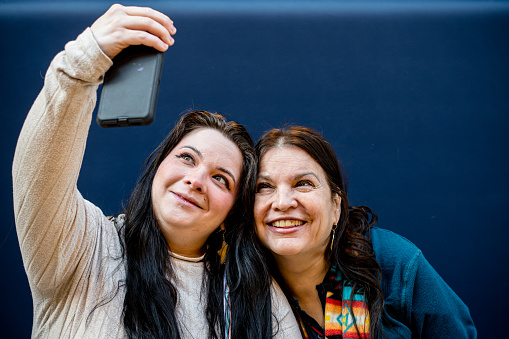 With smiles that light up the screen, two indigenous women lean in for a selfie, capturing a moment of shared joy and connection in the digital age.