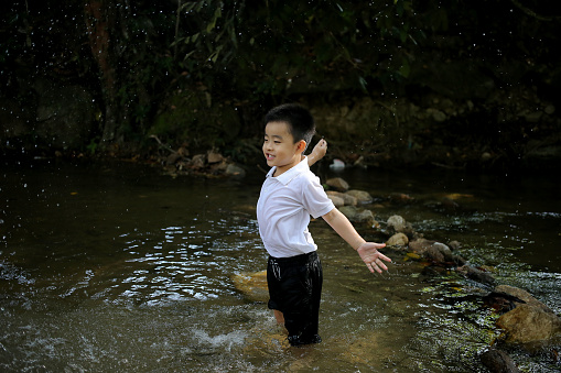 An Asian boy is at nature reserve forest playing with waterfall water