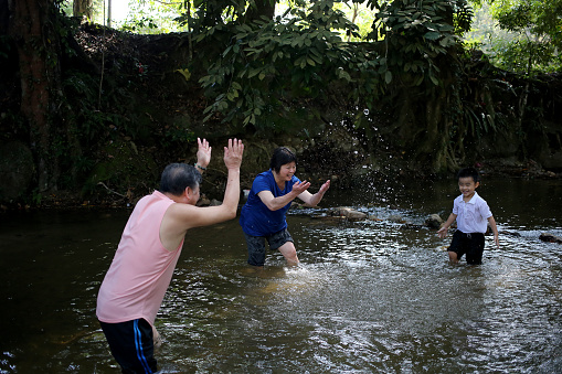 An Asian family is spending time together at nature reserve forest playing with waterfall water