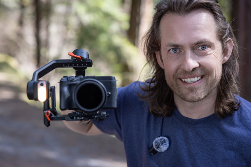 Content creator using a camera gimbal to film in nature with a blurred forest in the background