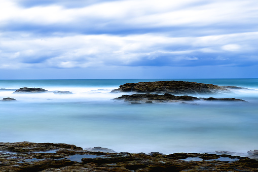 Landscape view of overcast sky view and sea wave crashing over rock on beach shore. Coffs Harbour, Australia.