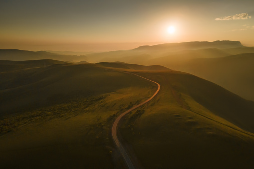 Road in the green hills at foggy sunrise. Gil-Su valley in North Caucasus, Russia. Beautiful summer landscape