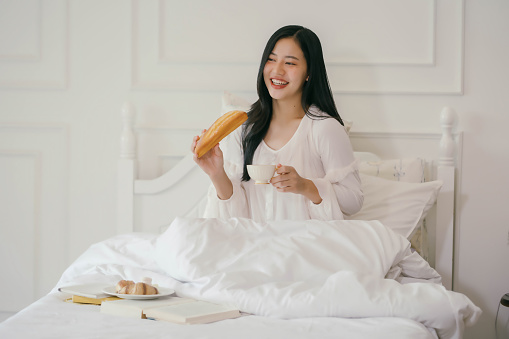 A woman is sitting on a bed with a plate of food and a cup of coffee. She is smiling and seems to be enjoying her meal
