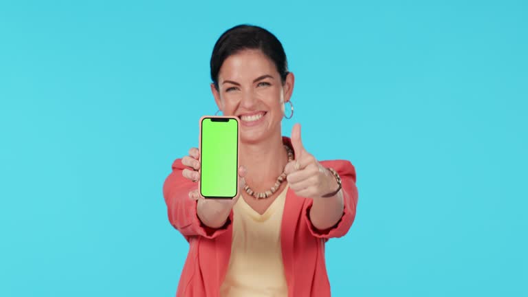 Green screen smartphone, okay thumbs up or happy woman with satisfaction feedback, mockup logo design or vote. Studio portrait, phone or person with ok icon, like or emoji gesture on blue background