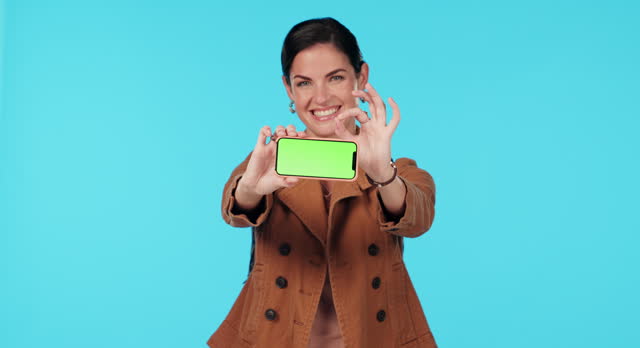 Green screen phone, okay and happy woman point at mobile app mockup, commercial agreement or branding space. Ok portrait, web media approval and studio person with success opinion on blue background