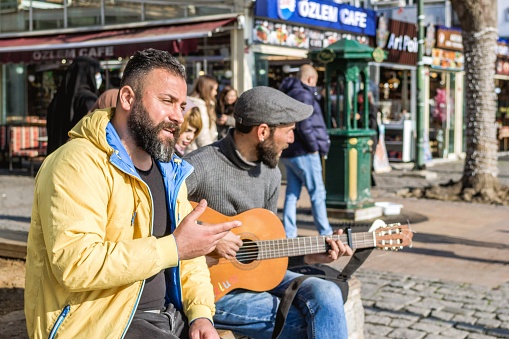 Istanbul, Turkey - December 29, 2022: Two men, one playing guitar and singing, the other listening intently on a city street corner.
