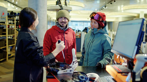A man and woman watching as a tech adjusts snowboard bindings in the equipment rental shop at the ski lodge at the base of the mountain in Niseko, Japan.