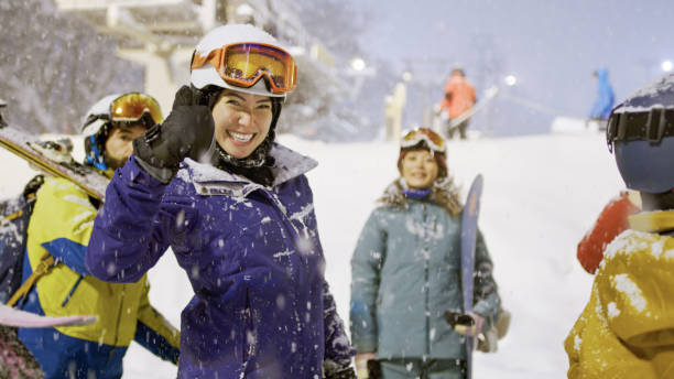 A group of skiers and snowboarders chatting and joking around at the base of the mountain in Niseko, preparing for a session of night skiing.