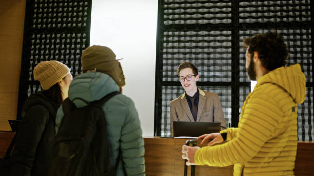 A young receptionist talking to three tourists standing from behind the counter inside a hotel in Niseko, Japan.