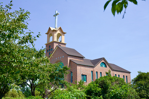 Goseong County, South Korea - July 30, 2019: Gajin Church, a notable brick building, features a cross atop a three-story tall bell tower, with its main building nestled below, situated near Gajin Port under a clear blue sky.
