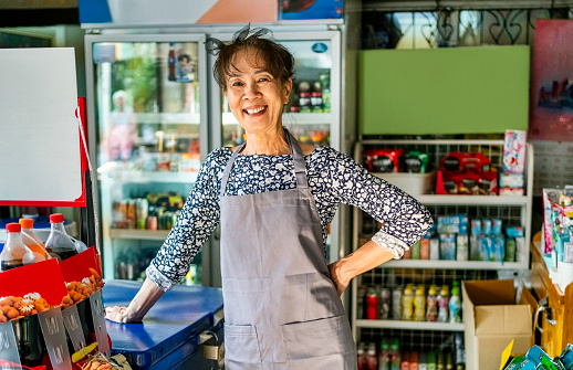 Portrait of a cheerful senior woman with apron standing behind counter at her local grocery shop
